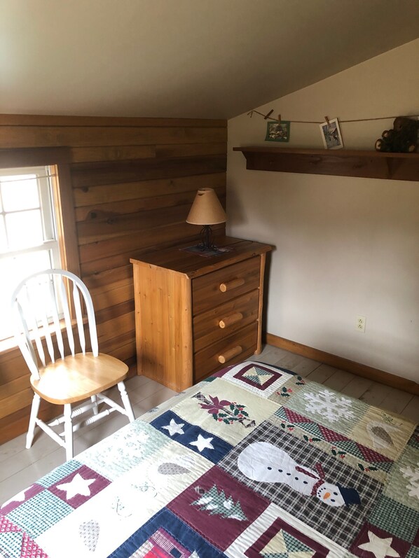 A cozy room with a wooden dresser, a white chair, and a colorful quilt on the floor. - Christmas Cabin in Hocking Hills (New Marshfield, Ohio)
