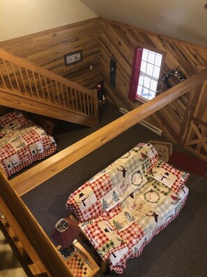 A loft-style room with a wooden ceiling and exposed beams, featuring two beds with festive bedding, a small window, and a wooden staircase. - Christmas Cabin in Hocking Hills (New Marshfield, Ohio)