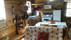 A cozy cabin interior with a wooden interior, a sofa with a festive pattern, a kitchen area with a stove and microwave, and a window with curtains. - Christmas Cabin in Hocking Hills (New Marshfield, Ohio)
