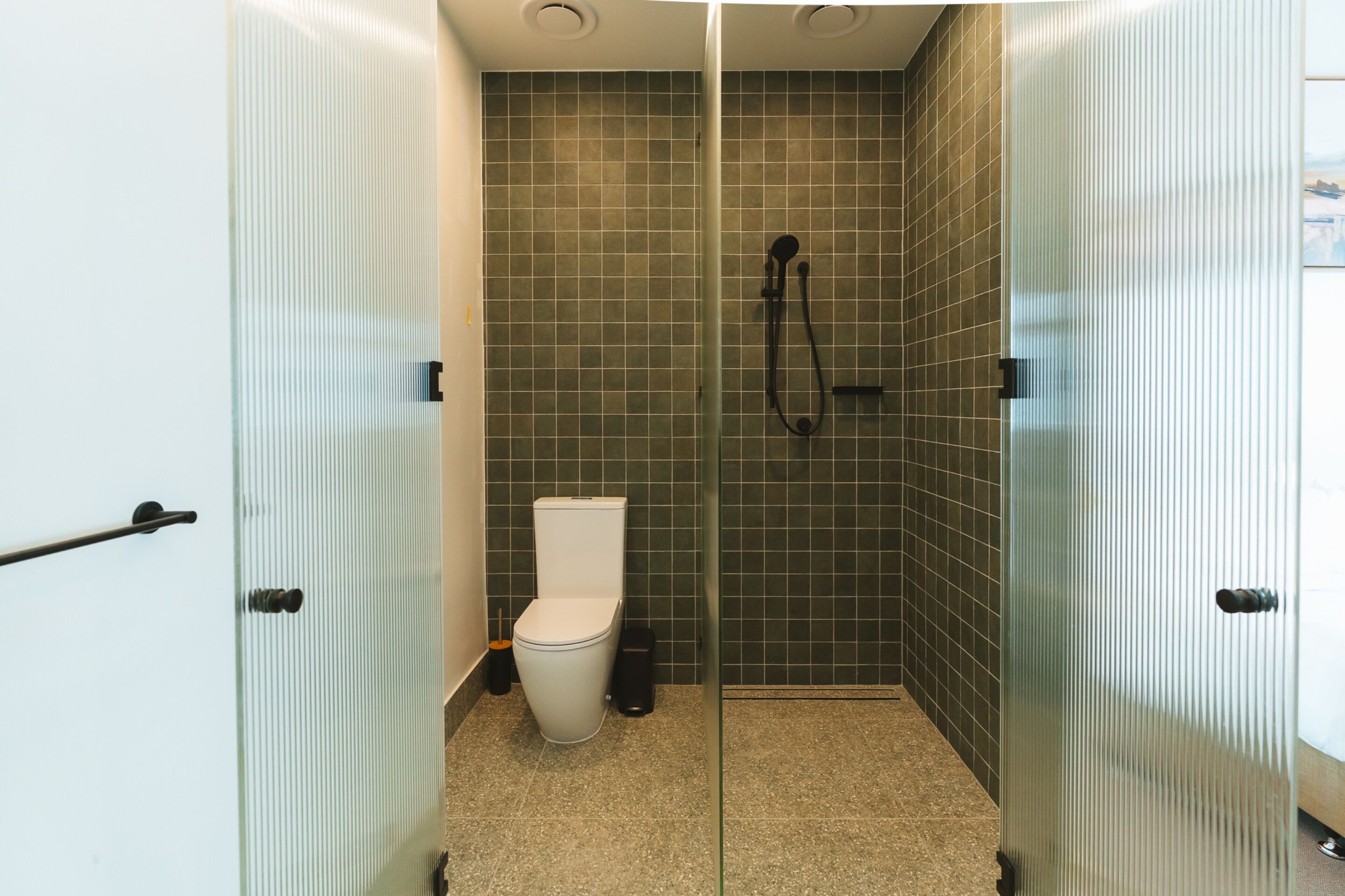 A bathroom with a glass partition, a toilet, a shower area, and a tiled wall.
