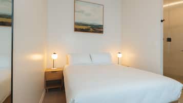 A neatly made bed with white linens, a bedside table with a lamp, and a painting on the wall.