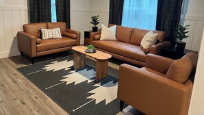 Een woonkamer met twee bruine leren banken, een houten salontafel en een zwart tapijt met witte patronen.