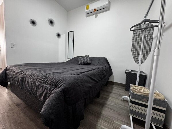 A bedroom with a bed, a mirror, an air conditioner, a radiator, and a storage unit.