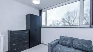 Quarto com uma janela grande, um guarda-roupa escuro e um sofá cinzento.