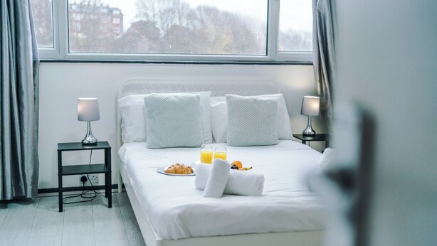 Cama bem arrumada com lençóis brancos, duas luminárias de cabeceira, um prato de croissants, uma garrafa de suco de laranja e uma toalha em um quarto de hotel.