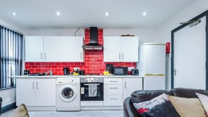 Uma cozinha moderna com armários brancos, painel de fundo vermelho e fogão preto.