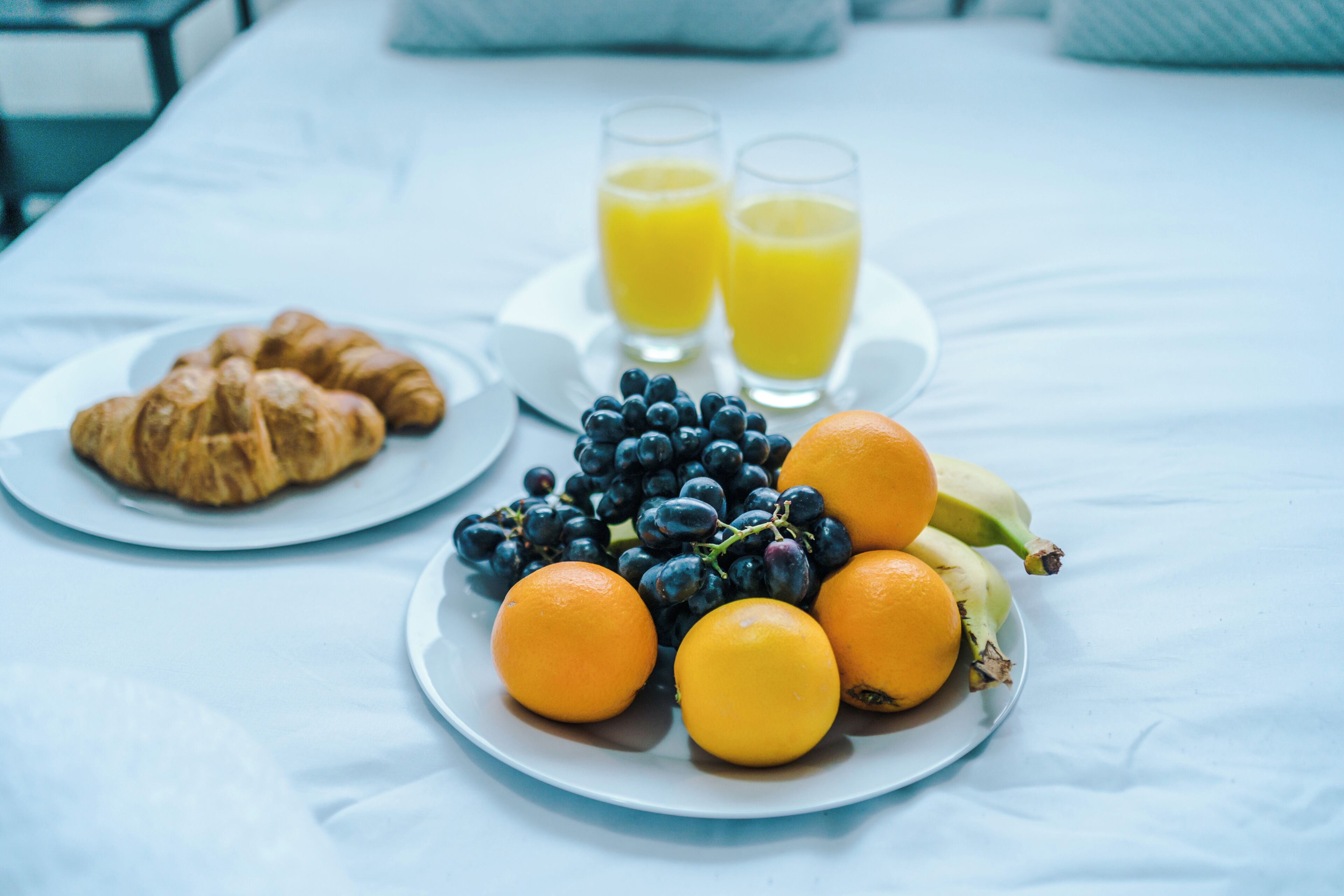 Une table de petit-déjeuner avec des croissants, des oranges, des bananes, des raisins et deux verres de jus d’orange.