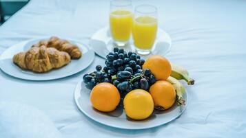 Une table de petit-déjeuner avec des croissants, des oranges, des bananes, des raisins et deux verres de jus d’orange.