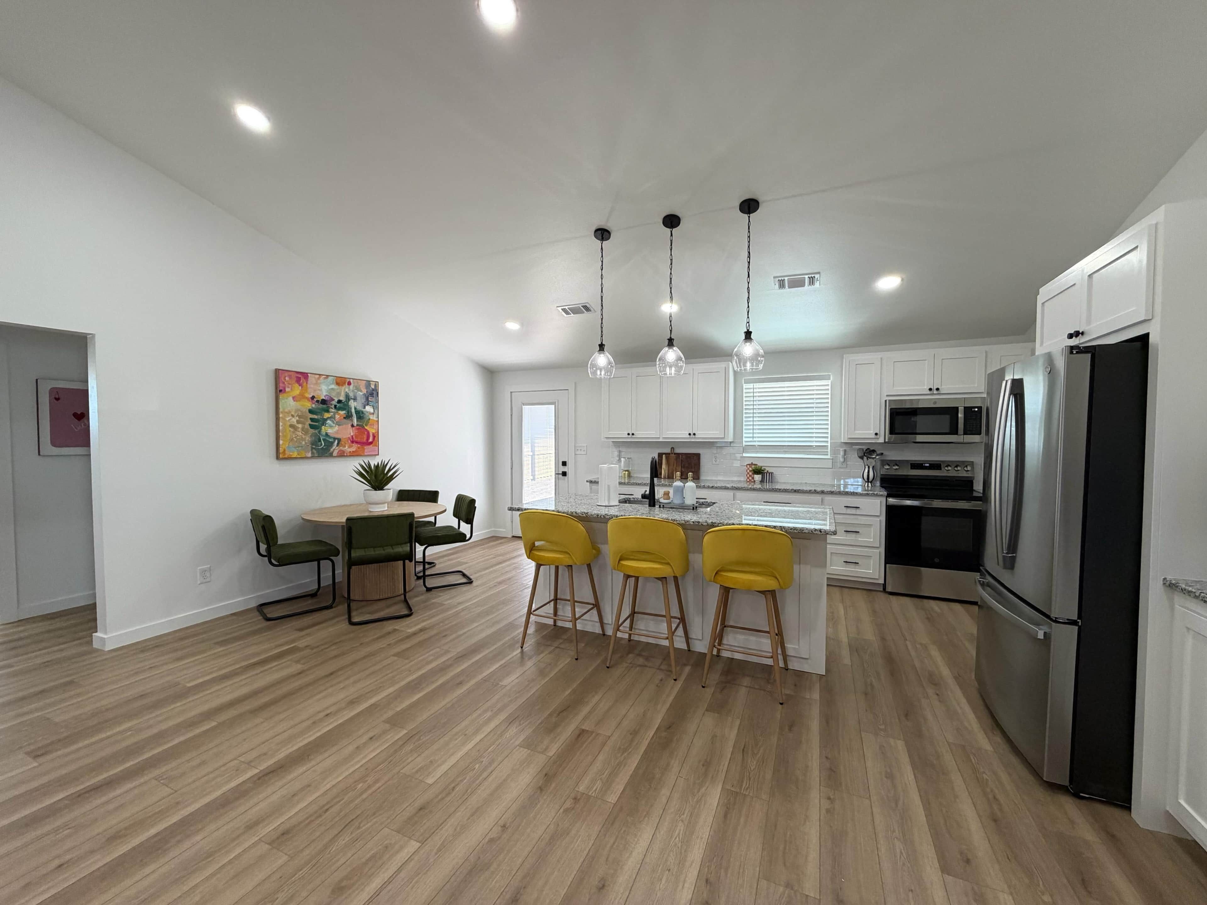 A spacious kitchen with white cabinets, a stainless steel refrigerator, and a central island with yellow bar stools.