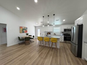 A spacious kitchen with white cabinets, a stainless steel refrigerator, and a central island with yellow bar stools. - Game Night Getaway - 3BR Near WinStar (Thackerville)