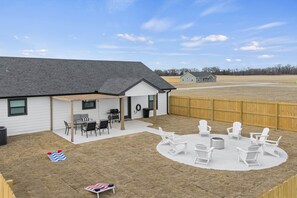 A backyard with a covered patio, outdoor seating, and a fire pit area. - Game Night Getaway - 3BR Near WinStar (Thackerville)