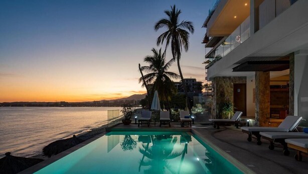 A modern hotel with a pool, lounge chairs, and palm trees. - Bucerias Beachfront Condo (Bucerías)