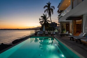 A modern hotel with a pool, lounge chairs, and palm trees. - Beach Apartment in Buceria (Bucerías)
