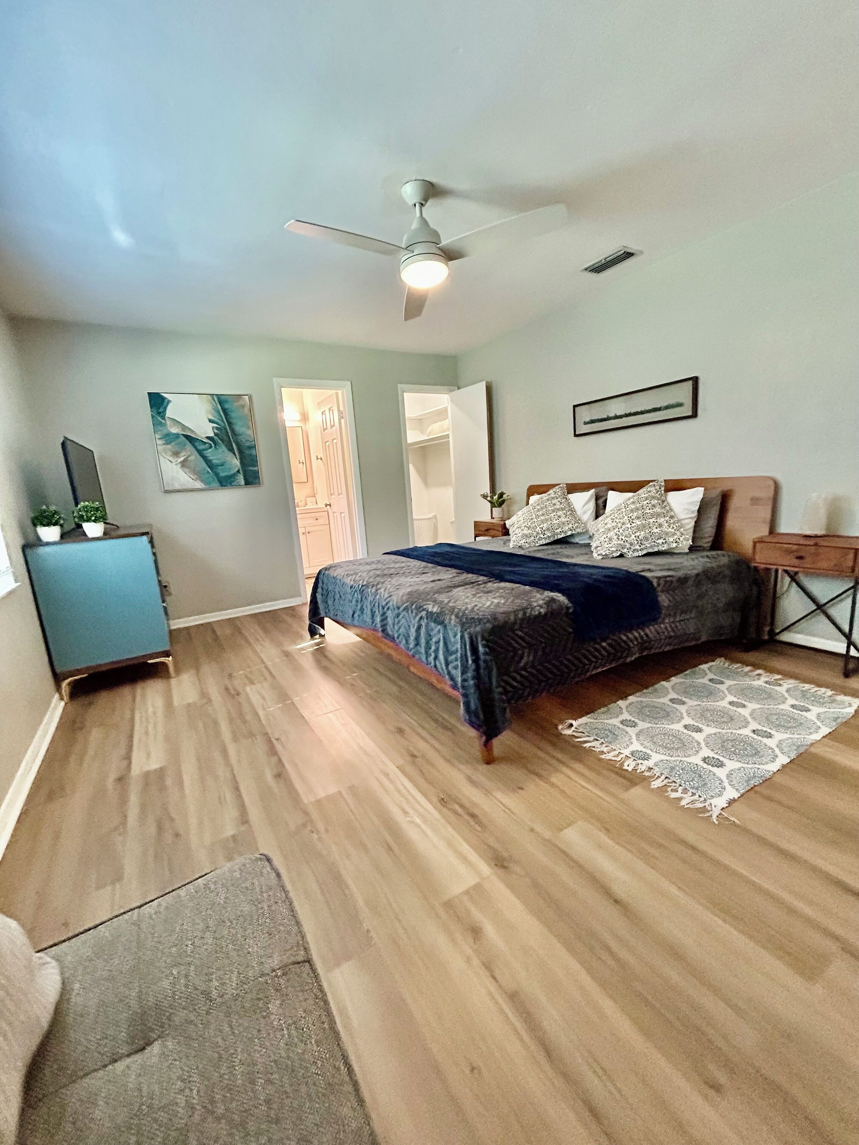 A bedroom with a bed, a ceiling fan, a dresser, and a door leading to another room.