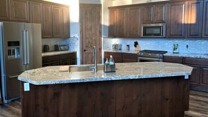 A modern kitchen with dark wood cabinets, a granite countertop island, stainless steel appliances, and a large window above the sink. - EARLY CHECK IN/OUT 1PM Luxury Home on POND in Torreon-Hot Tub & Kids Zone (Show Low)