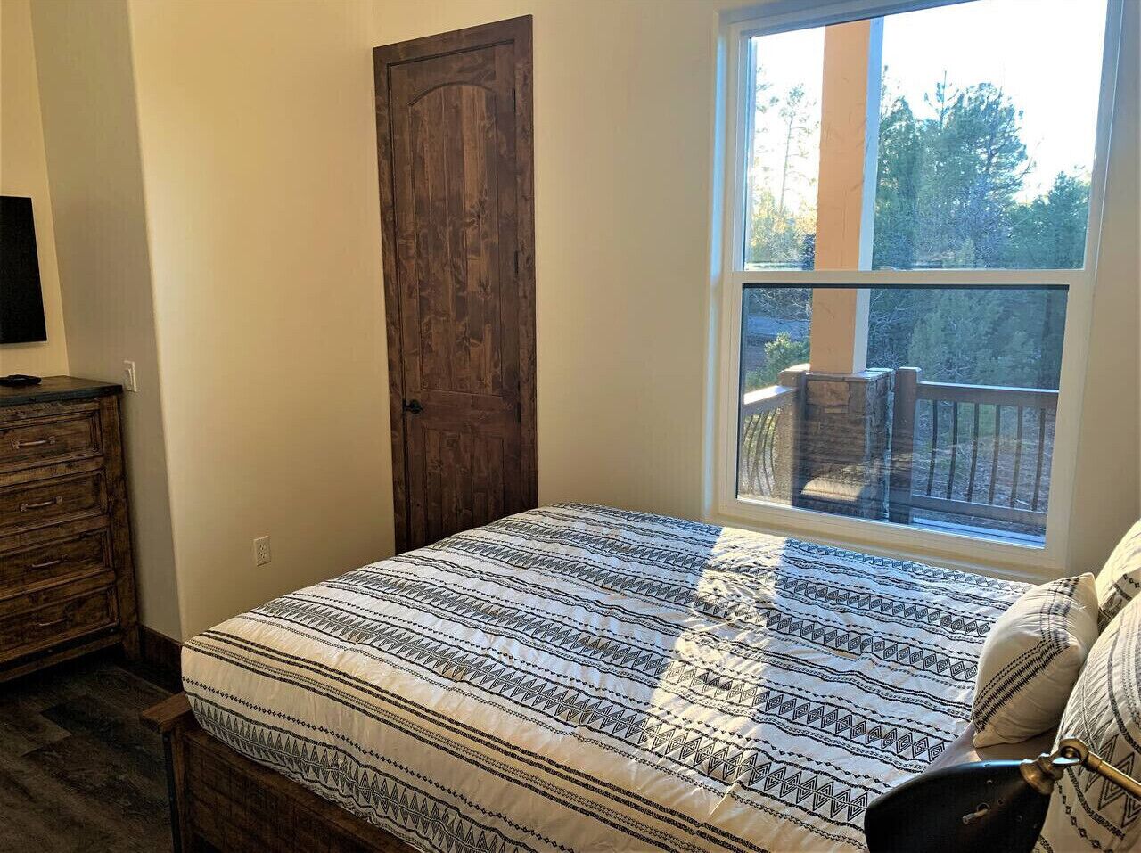 A bedroom with a bed, a dresser, a window with a view of trees, and a door.