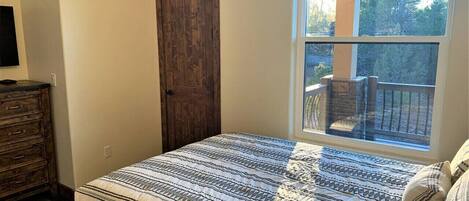 A bedroom with a bed, a dresser, a window with a view of trees, and a door.