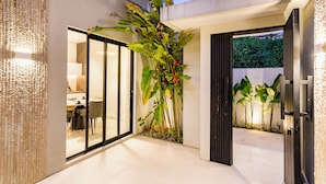 A modern interior with a glass door leading to a dining area, a large plant, and a well-lit entrance. - Anoya Boutique Villa (Kerobokan)