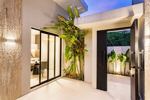 Interior moderno com porta de vidro que dá para uma sala de jantar, uma planta grande e uma entrada bem iluminada.