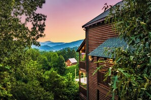 A wooden cabin with a balcony overlooking a forested valley and distant mountains. - Luxe 5* Retreat~NovDeals~GmRm~PS5~Views~HotTub (Gatlinburg)