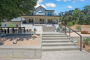 A two-story house with a front porch, a staircase leading to the entrance, and a patio area with outdoor furniture. - Private Oasis in Healdsburg: Pool, Spa & Views (Healdsburg)