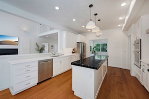 A modern kitchen with white cabinetry, a black countertop island, stainless steel appliances, and a wooden floor. - Private Oasis in Healdsburg: Pool, Spa & Views (Healdsburg)