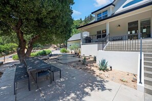 Eine Terrasse mit Tisch und Stühlen, ein Baum und ein Haus mit Balkon.