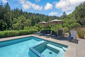 Une piscine entourée d’une végétation luxuriante et d’arbres, avec des chaises longues et des parasols à proximité.