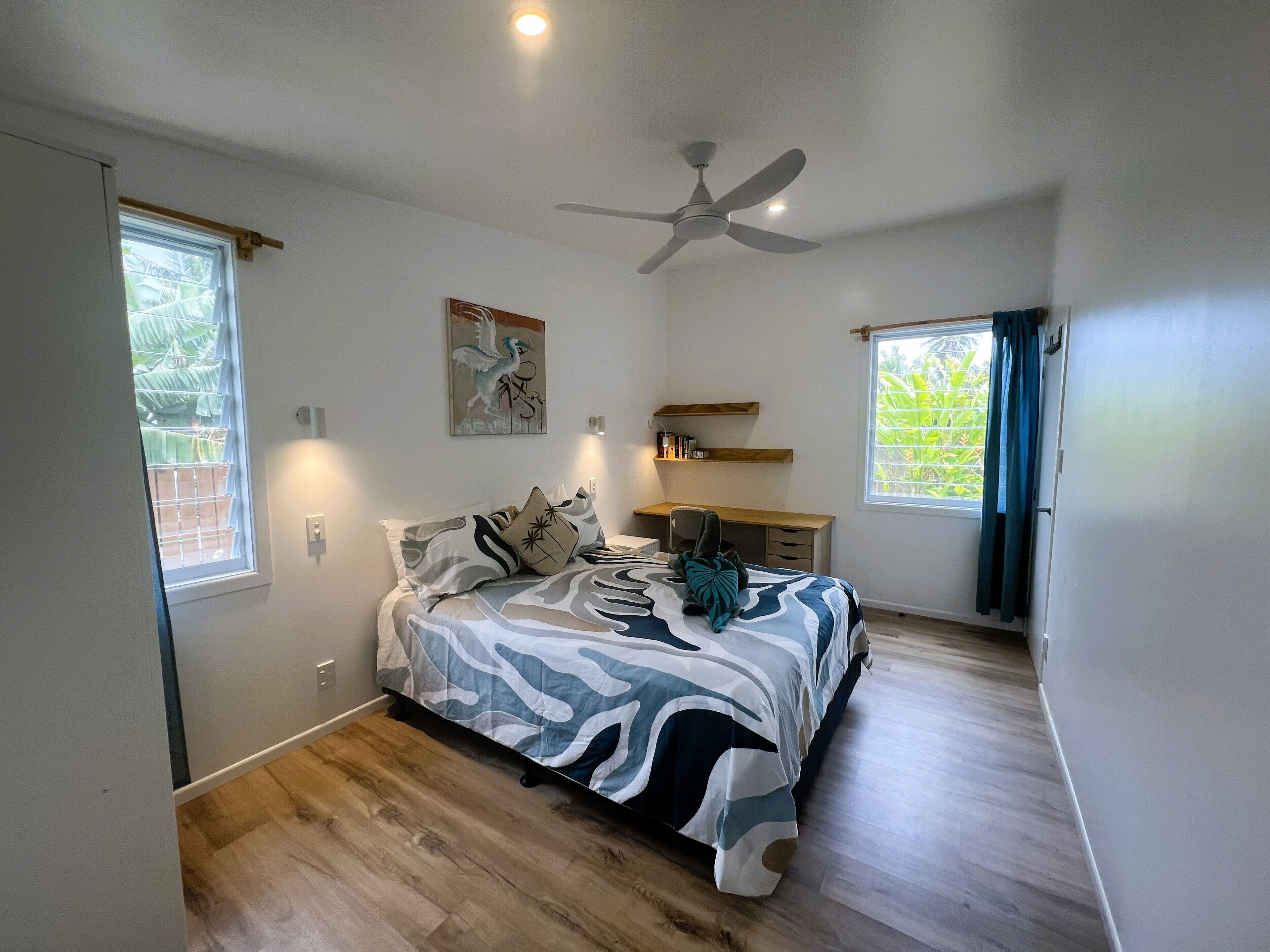 A bedroom with a bed, a desk, a ceiling fan, and a window with curtains.