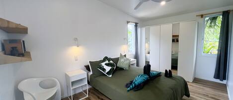 A modern bedroom with a bed, a ceiling fan, a nightstand, a white chair, and a window with curtains.