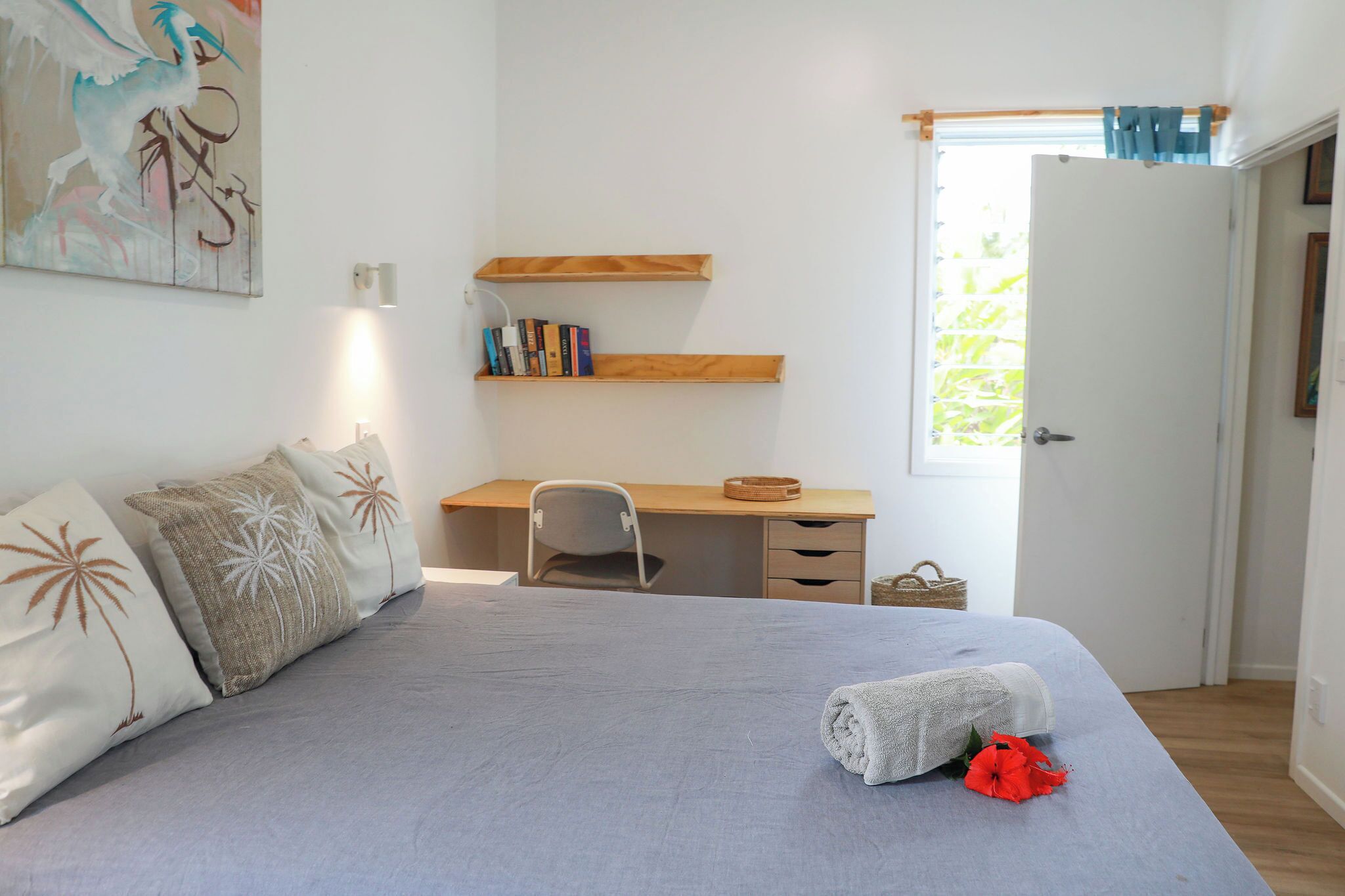 A bedroom with a bed, a desk, and a chair. There are books on the desk and a painting on the wall.
