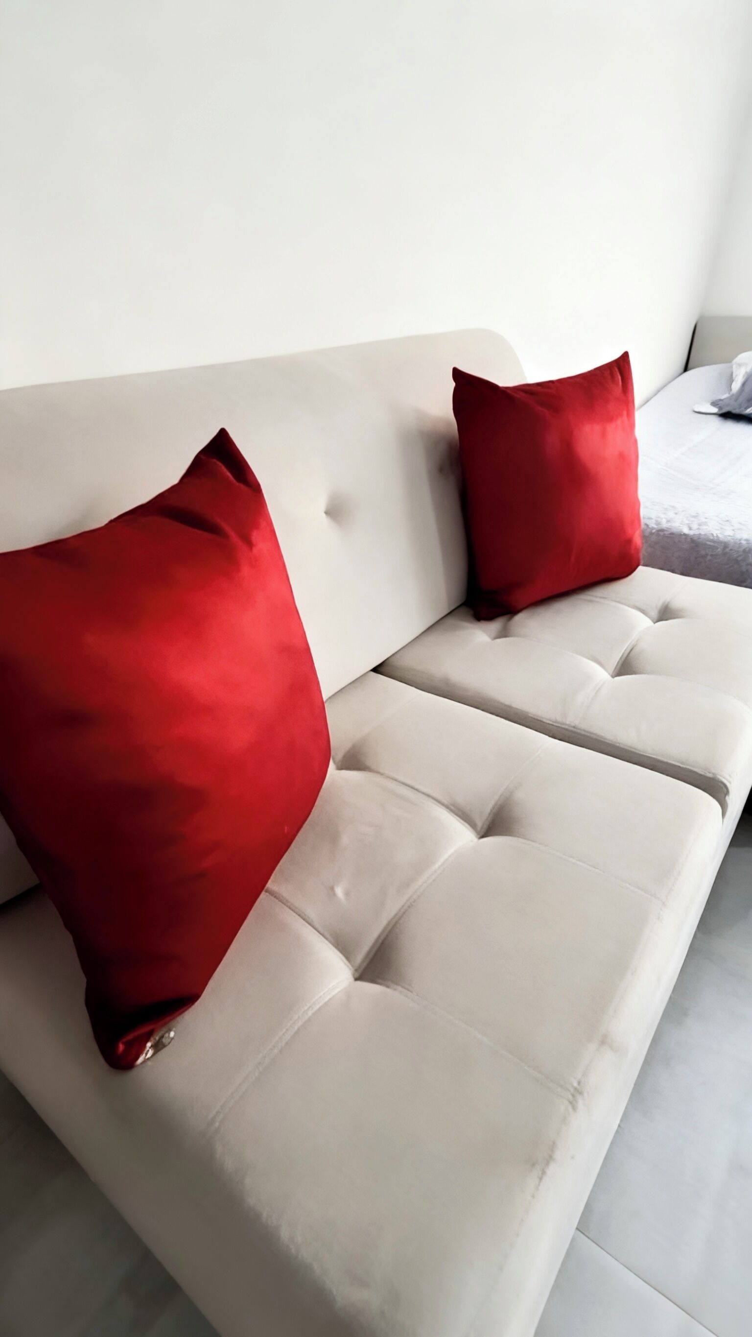 A beige sofa with two red pillows and a grey blanket.