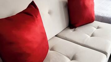 A beige sofa with two red pillows and a grey blanket.