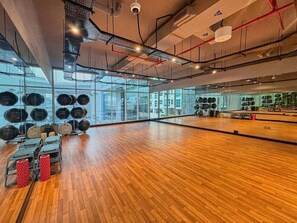 Ett rymligt gym med trägolv, träningsutrustning och stora fönster med utsikt över staden.