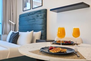 A hotel room with a bed, a dining table with waffles and fruit, and two glasses of orange juice. - Cozy Marina Studio w/ Balcony (Dubai)