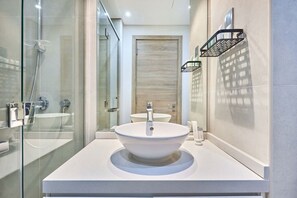 A modern bathroom with a glass shower enclosure, a white sink, and a wooden door. - Cozy Marina Studio w/ Balcony (Dubai)