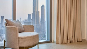 A modern living room with a large window offering a city skyline view, a plush armchair, and a set of curtains. - Spacious 4-Bedroom Downtown Apartment with Burj Views (Dubai)