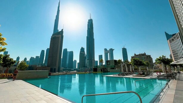 A swimming pool with a city skyline in the background, including a prominent skyscraper. - Spacious 4-Bedroom Downtown Apartment with Burj Views (Dubai)