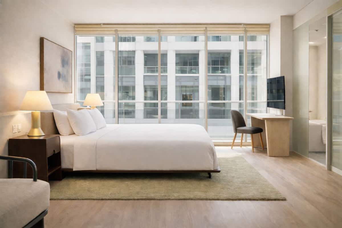 Una habitación de hotel moderna con una cama grande, dos lámparas de noche, un escritorio y una silla.