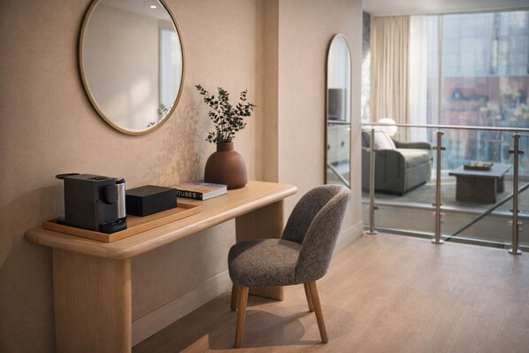 A modern hotel room with a wooden desk, a coffee maker, a book, and a vase with a plant.