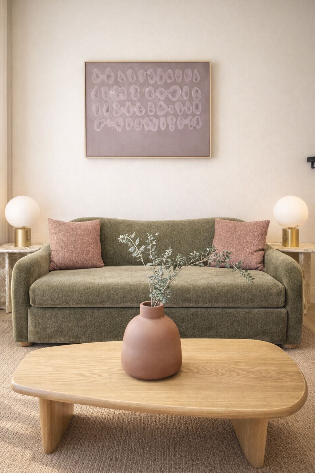 A living room with a green sofa, two pink pillows, a vase with branches, and two side tables with lamps.