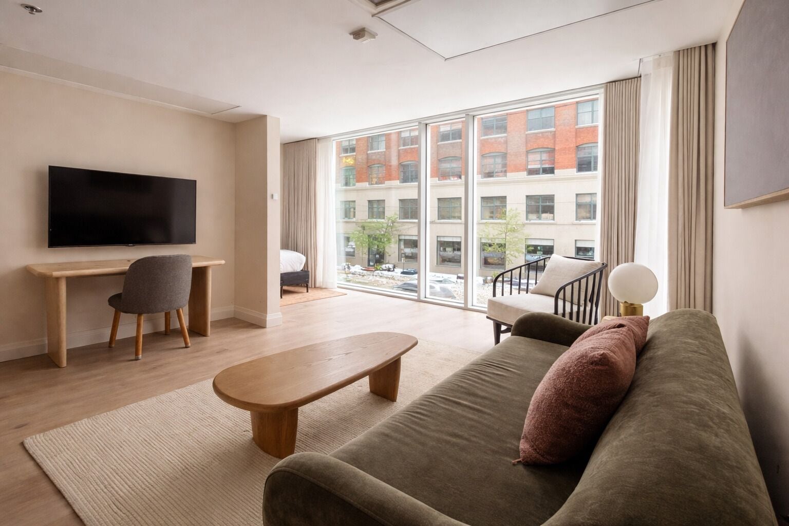 A modern living room with a large window, a flat-screen TV, a sofa, a coffee table, and a desk with a chair.