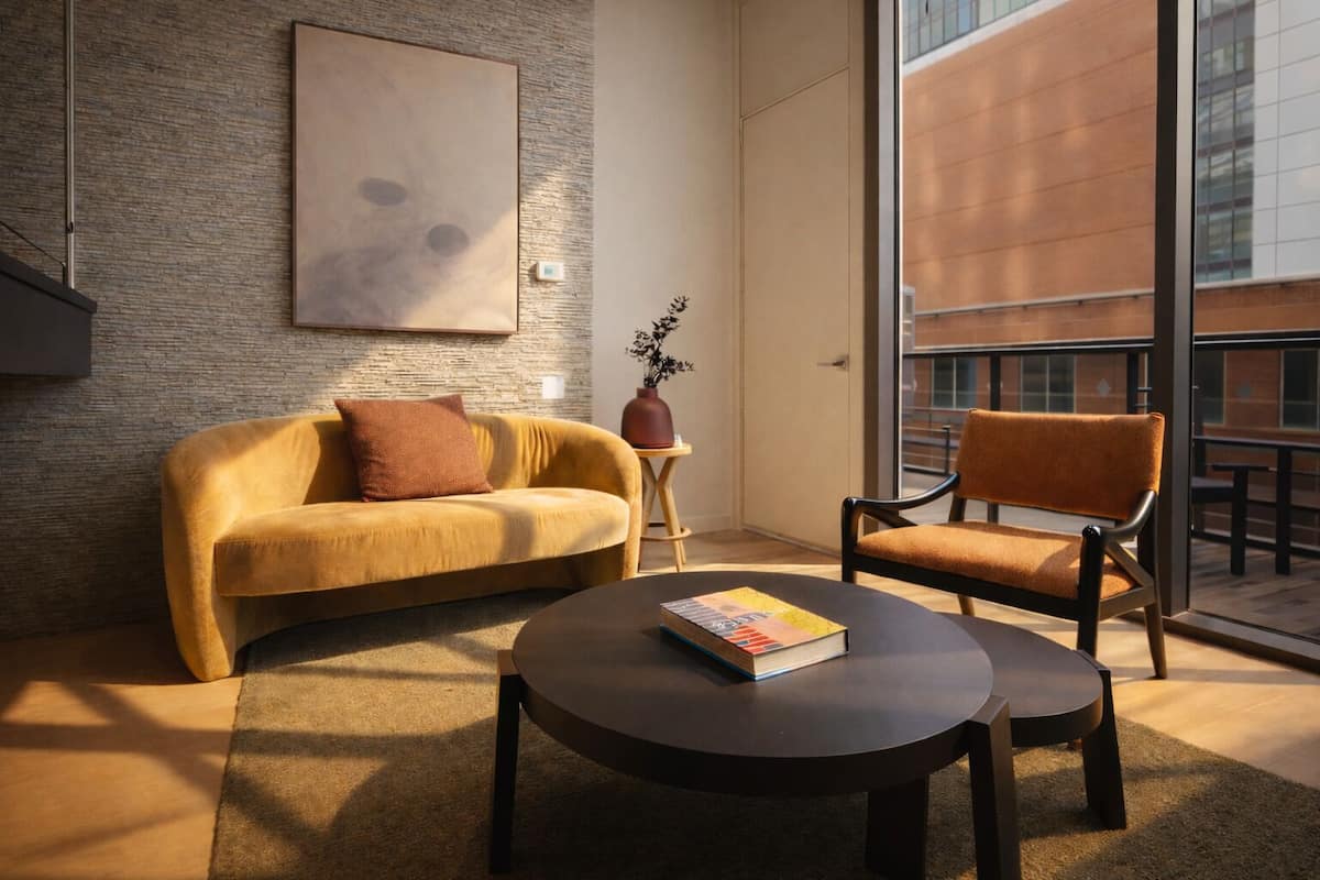 Una sala moderna con un sofá amarillo, una mesa de centro redonda y un sillón marrón.
