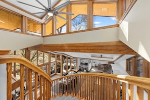 Una escalera de madera de varios niveles con un ventilador de techo, ventanas amplias y vistas al exterior.