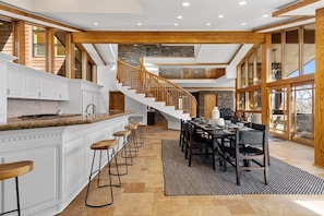 Una cocina amplia con una isla central, un comedor con una mesa larga y una escalera que lleva a un nivel superior.
