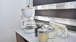 Uma bancada de cozinha com uma cafeteira, potes de açúcar e especiarias, e uma pequena tigela.