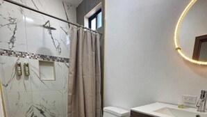 Uma casa de banho moderna com chuveiro em cabine de vidro, sanita, toucador com espelho e uma pequena janela.