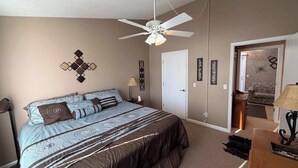 Een slaapkamer met een bed, plafondventilator, wanddecoraties en een deur naar een andere kamer.