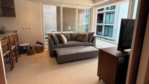 Een moderne woonkamer met een grijze bank, een houten bureau en een groot raam.