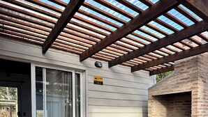 Puuinen terassi, jossa on pergola, grillauspaikka sekä pöytä ja penkit.